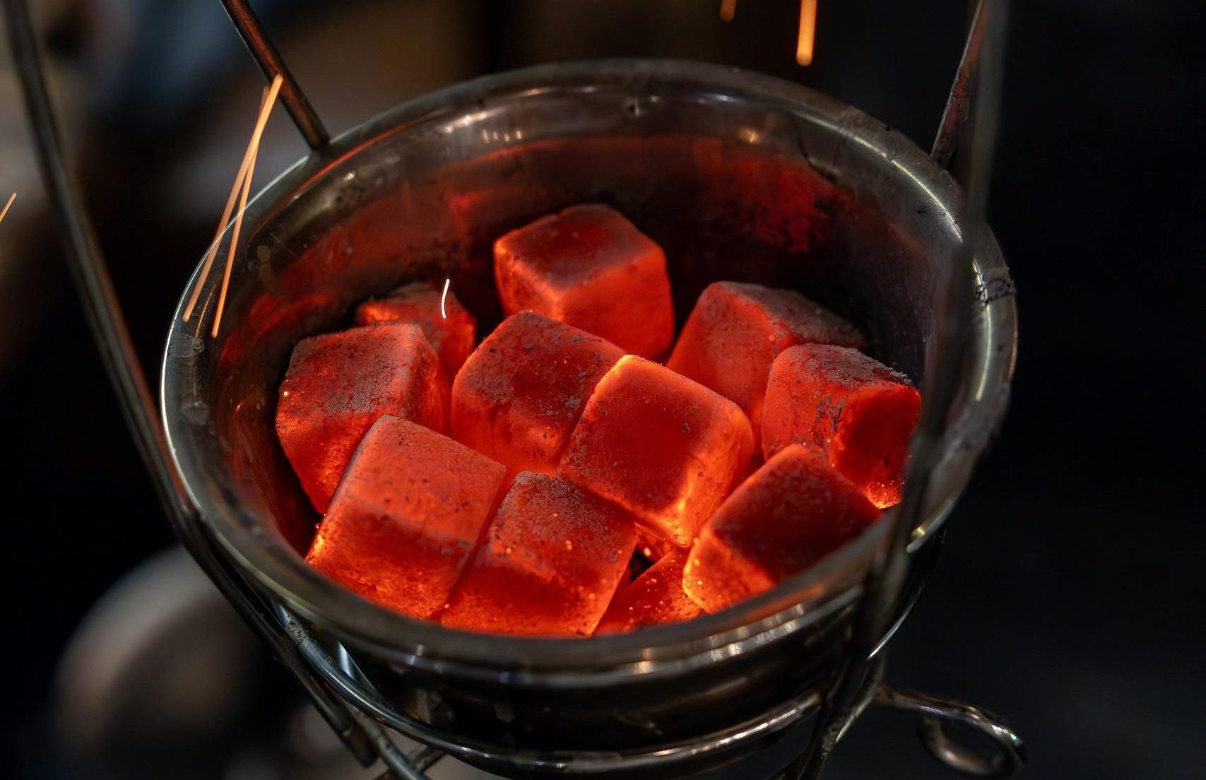 Close-up of red hot charcoal cubes emitting sparks in a metal holder.